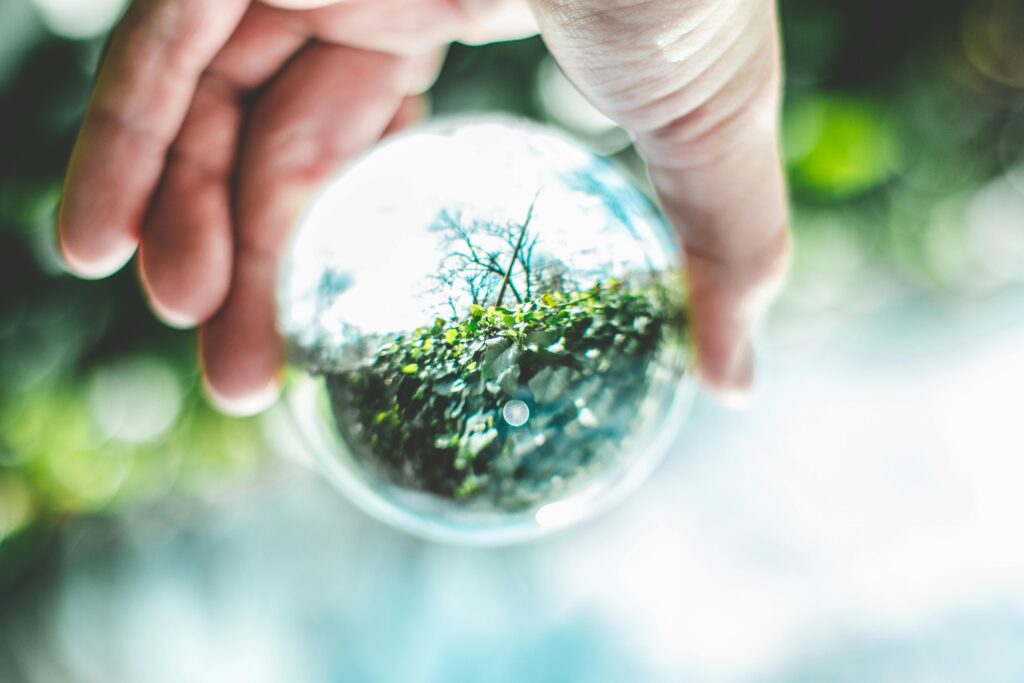 Hand holding a lensball reflecting vibrant green outdoor scenery. Perfect for nature and reflection themes.